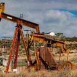 A rusty oil pumpjack situated in a desert-like landscape under a partly cloudy sky.